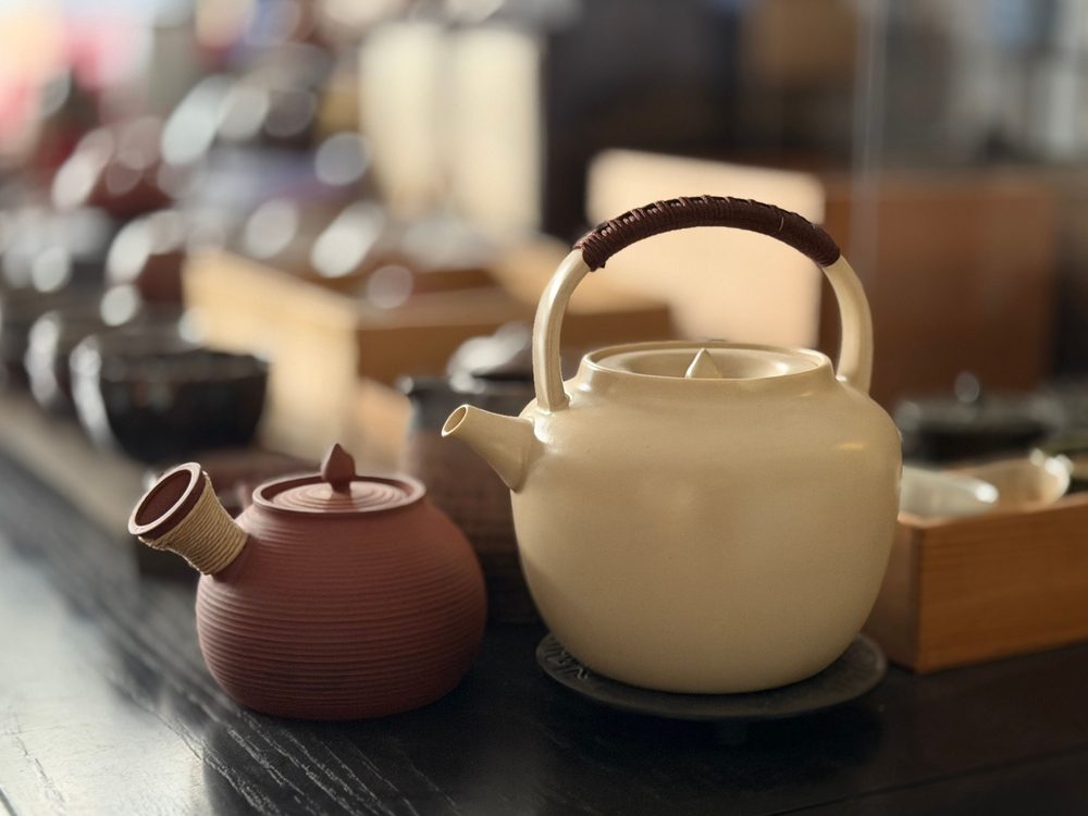 Ceramic teapots on a dark counter in a warm, softly lit tea room.