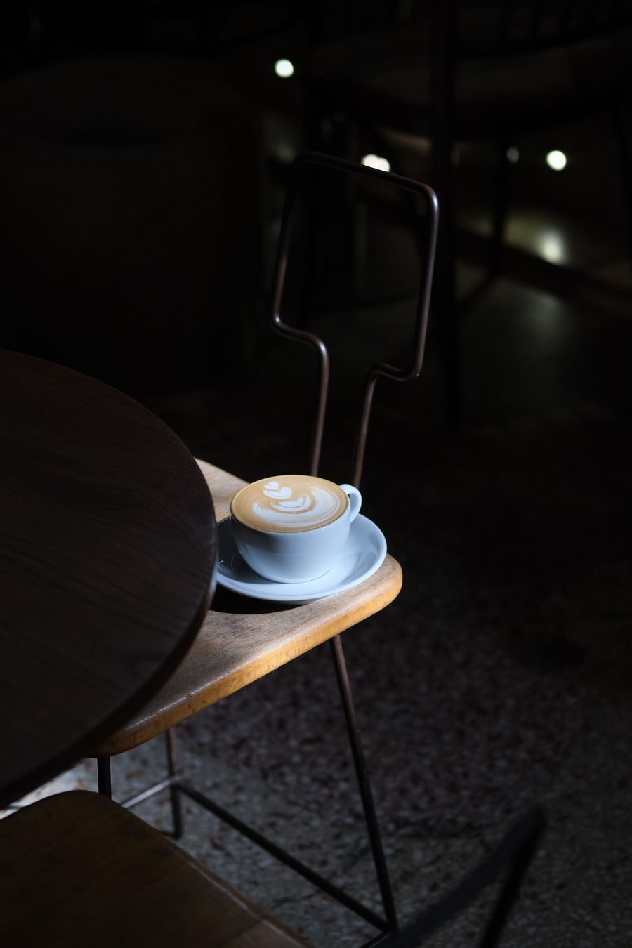 A cup of coffee with latte art on a wooden table, dimly lit café interior.